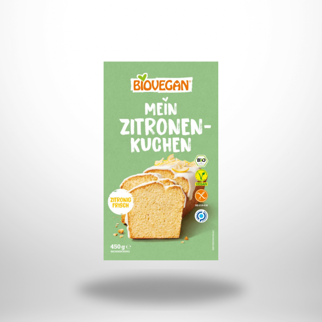 Grüne 450-g-Faltschachtel „Biovegan Mein Zitronenkuchen“ neben angeschnittenem, glasiertem Zitronenkastenkuchen.